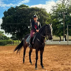 Marcele montada num cavalo preto, numa pista de areia